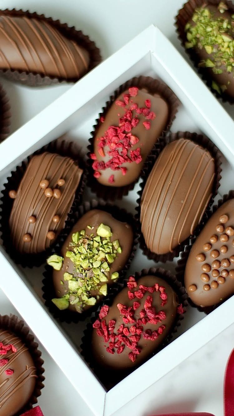 Assorted chocolate-covered treats with raspberry and pistachio toppings in a white gift box