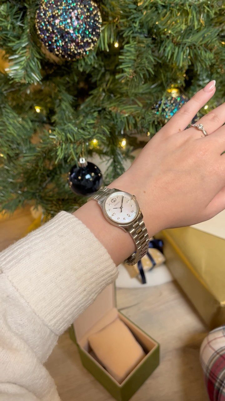 Silver wristwatch on a woman's wrist in front of a decorated Christmas tree