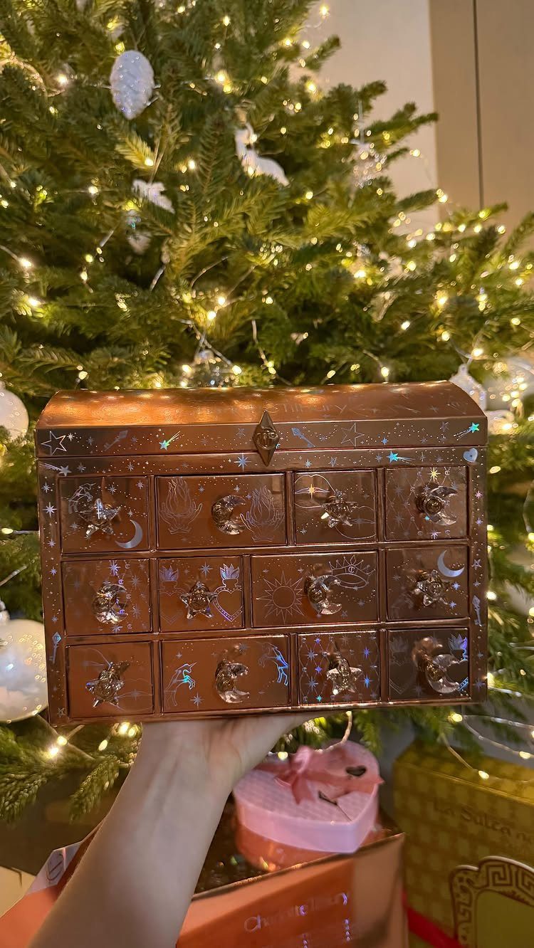 Rose-gold decorative chest with small drawers held in front of a lit Christmas tree
