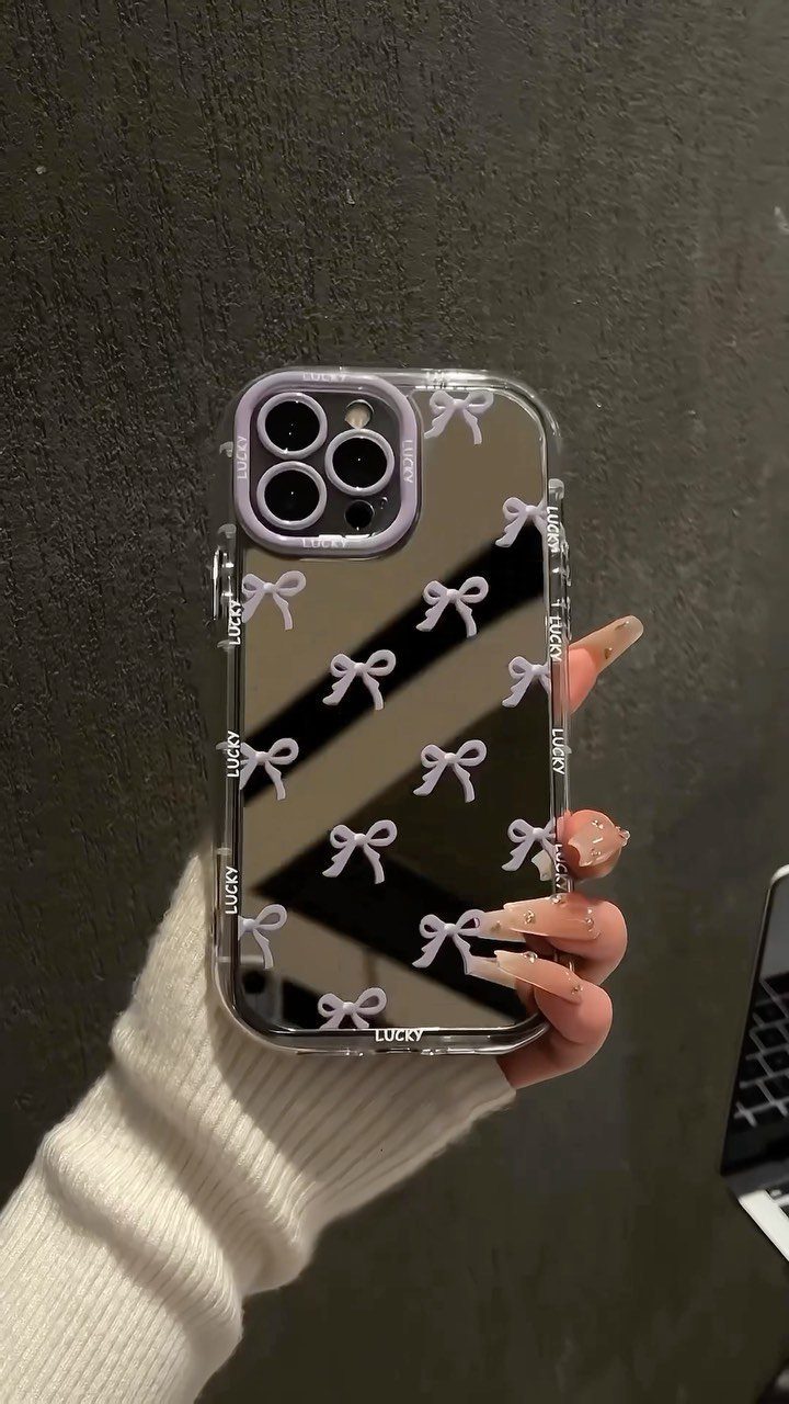Smartphone with a clear case decorated with purple bows held by a hand.