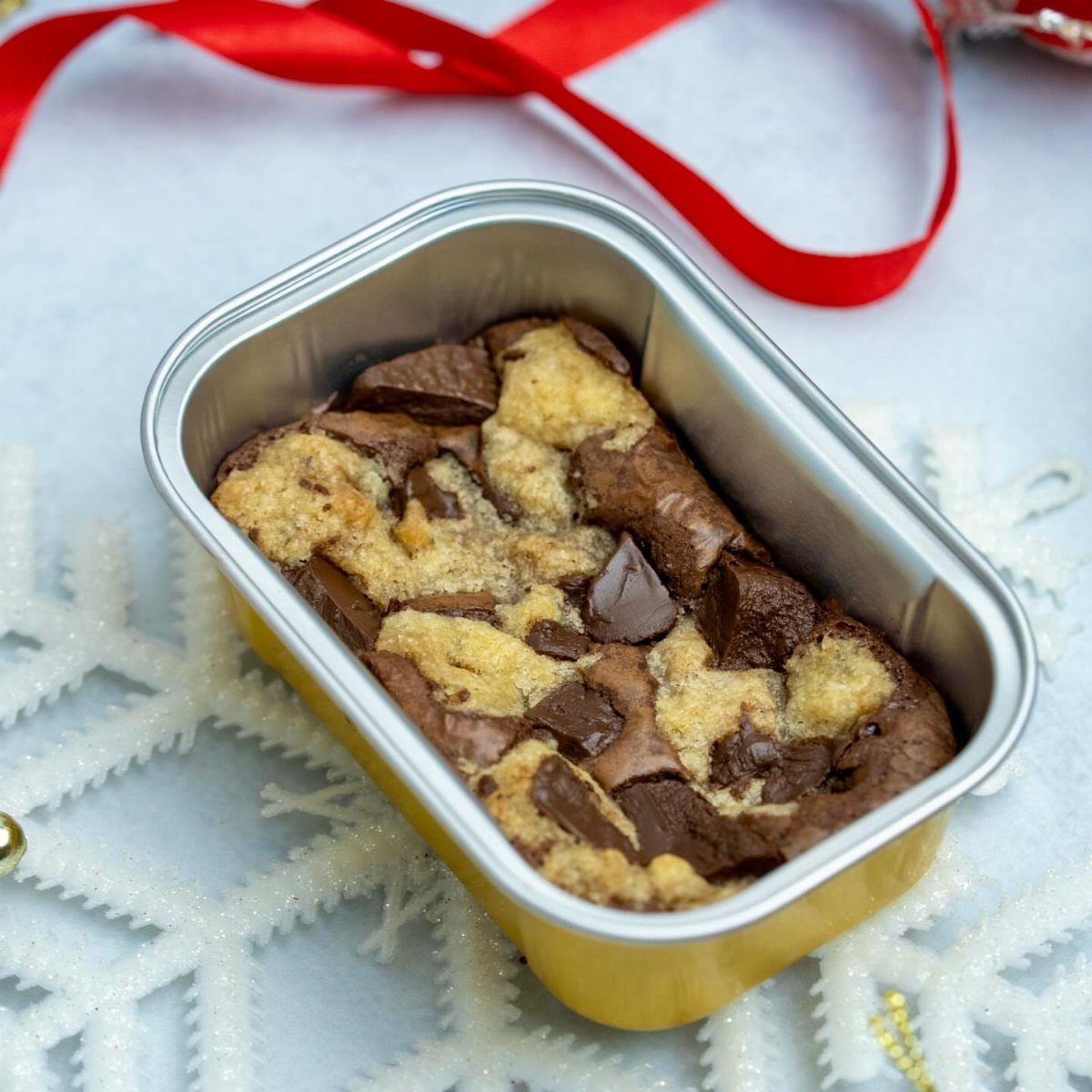 Chocolate chip brownies in a yellow tin with red ribbon and snowflakes.