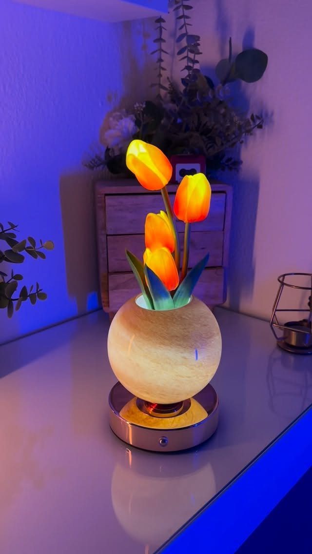 Glowing orange tulip lamp in a round stone vase on a reflective surface