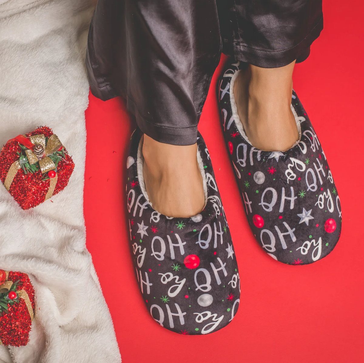 Plush grey Christmas slippers with Ho Ho Ho text on a red background