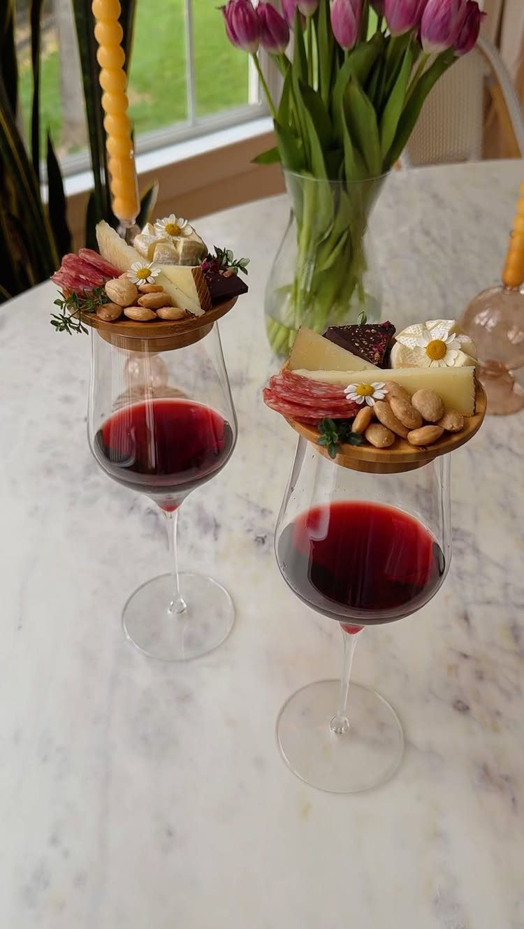 Two red wine glasses with wooden snack platters on a marble table