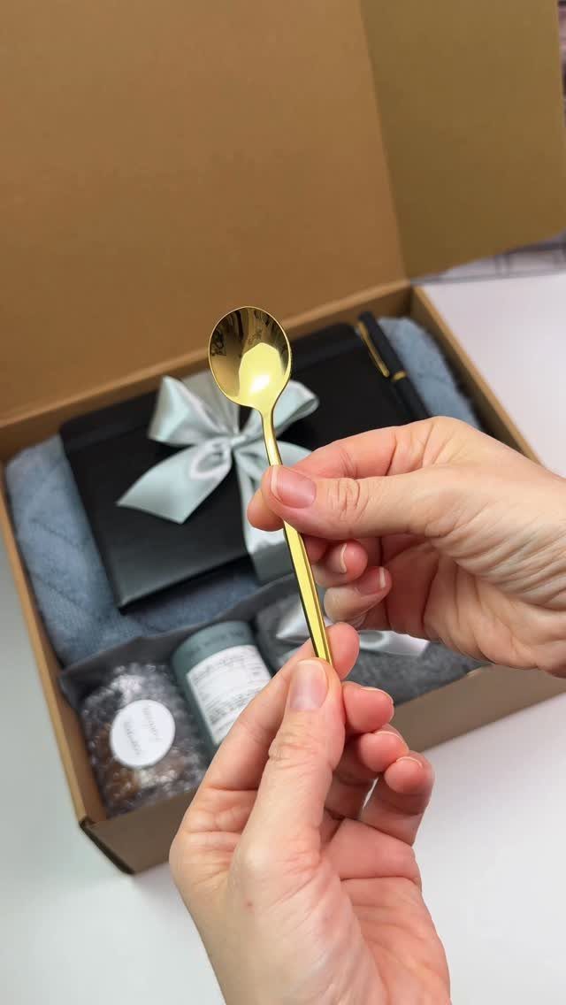 Gold spoon held over a curated gift box with treats and a ribbon.