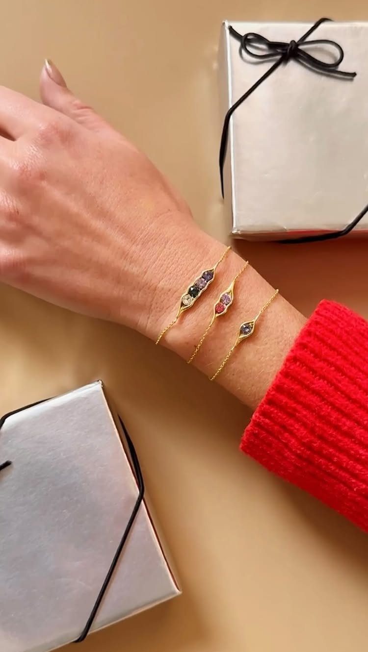 Three gold gemstone bracelets on a wrist next to white wrapped gift boxes