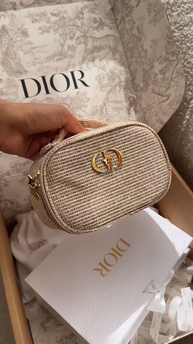 Beige woven Dior cosmetic pouch held over a branded Dior gift box.