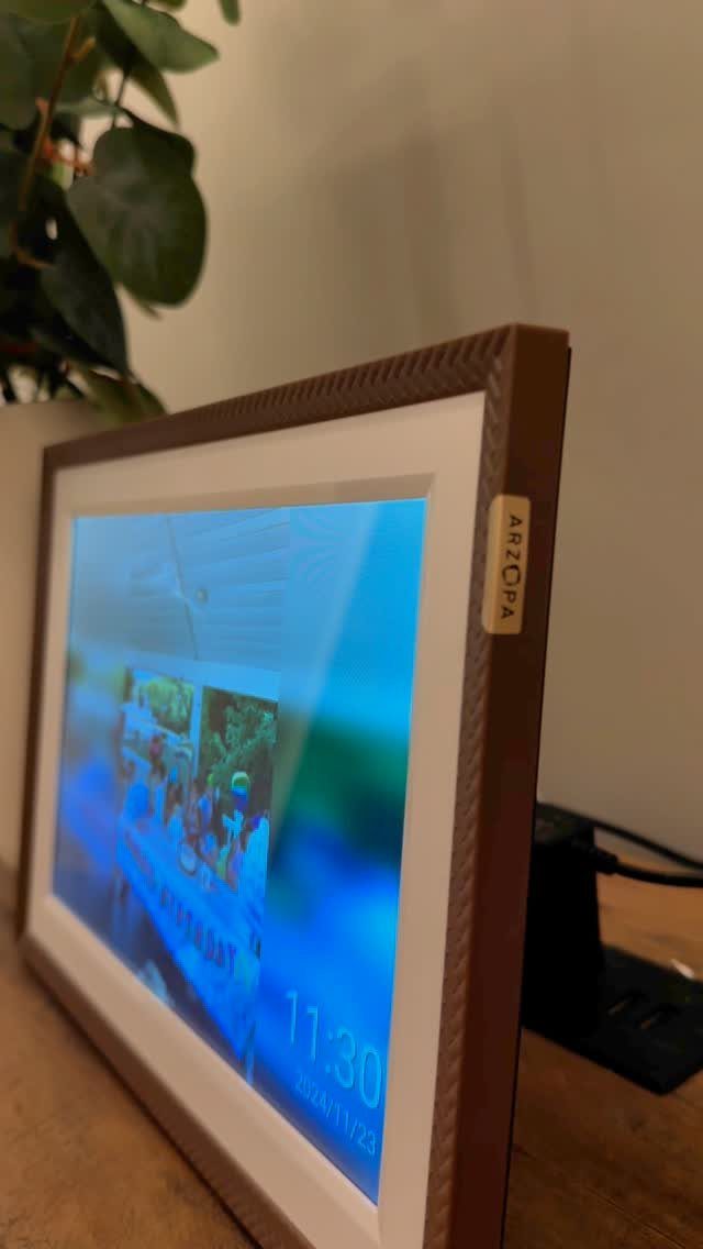 Digital photo frame with brown border displaying a picture and time on wooden table