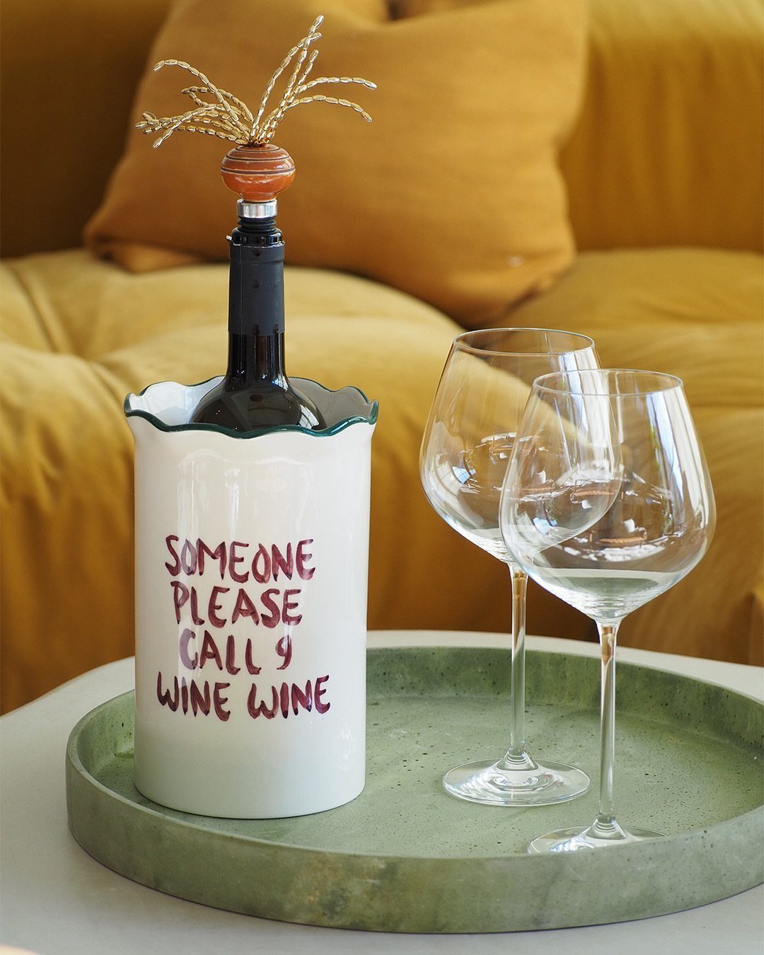 Wine chiller with funny text and two clear wine glasses on a green tray.