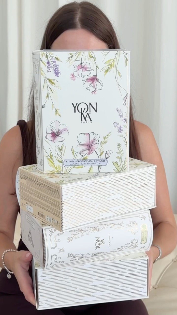 Woman holding a stack of Yonka Paris skincare product boxes with floral designs.