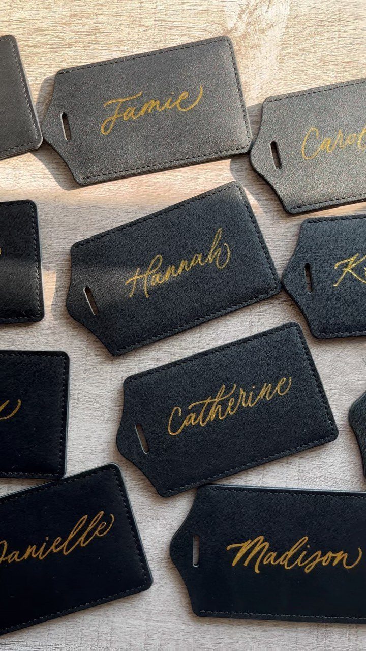 Black leather luggage tags with gold personalized names on a wooden background