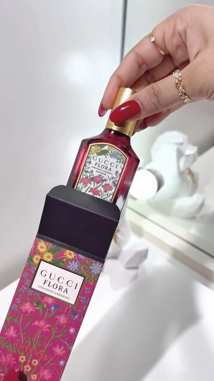 Gucci Flora perfume bottle in floral packaging held by a hand with red nails.