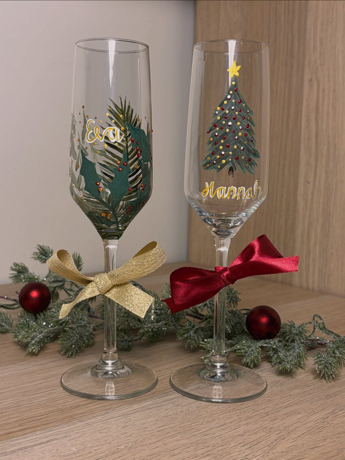 Two personalized champagne flutes with Christmas designs and names on a wooden table.