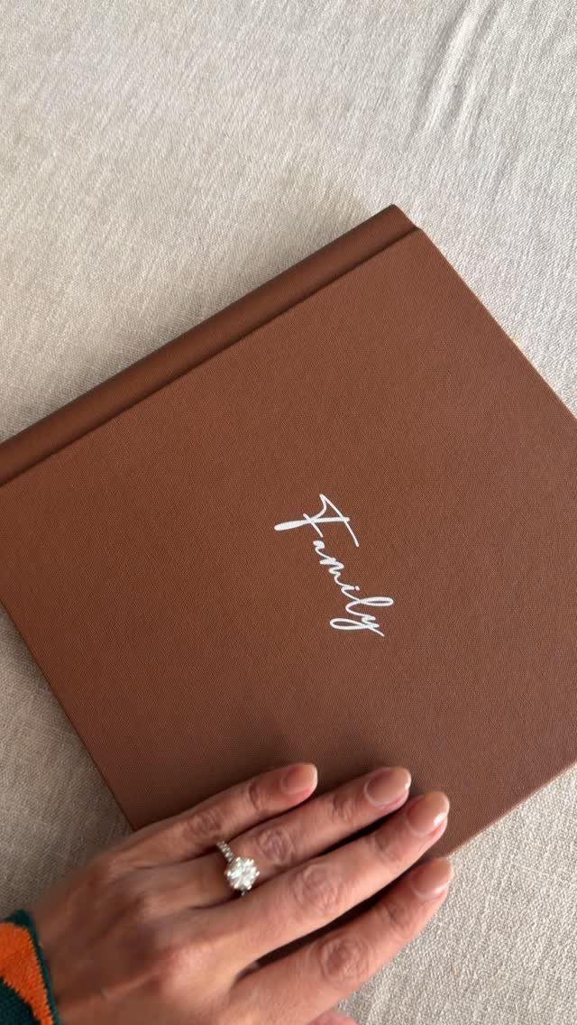 Brown fabric photo album with white Family script and a hand resting on it.