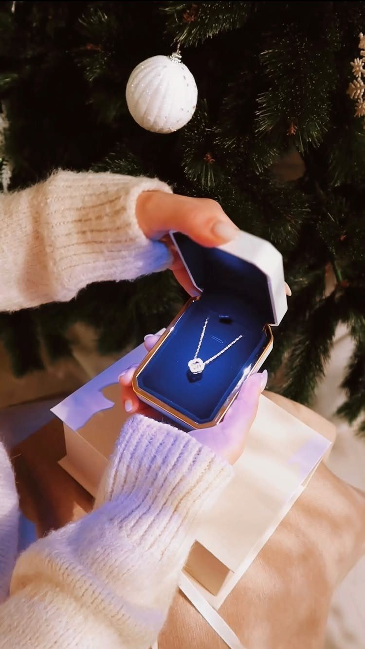 Silver necklace with a pendant in a blue box held near a Christmas tree
