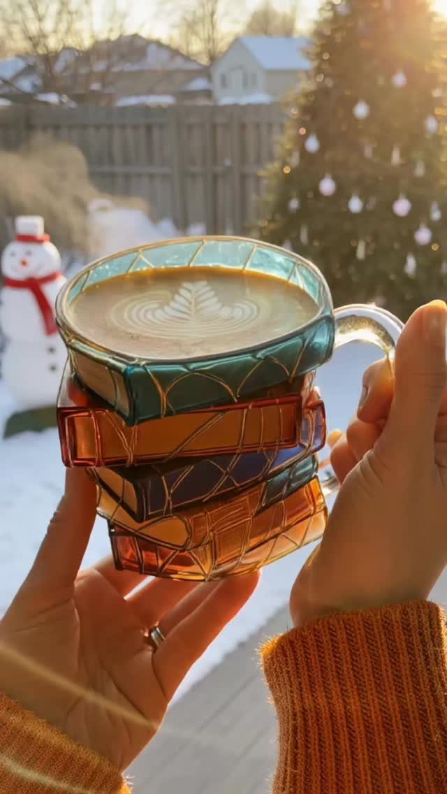 Stacked colorful geometric glass mugs with latte art in a snowy winter setting