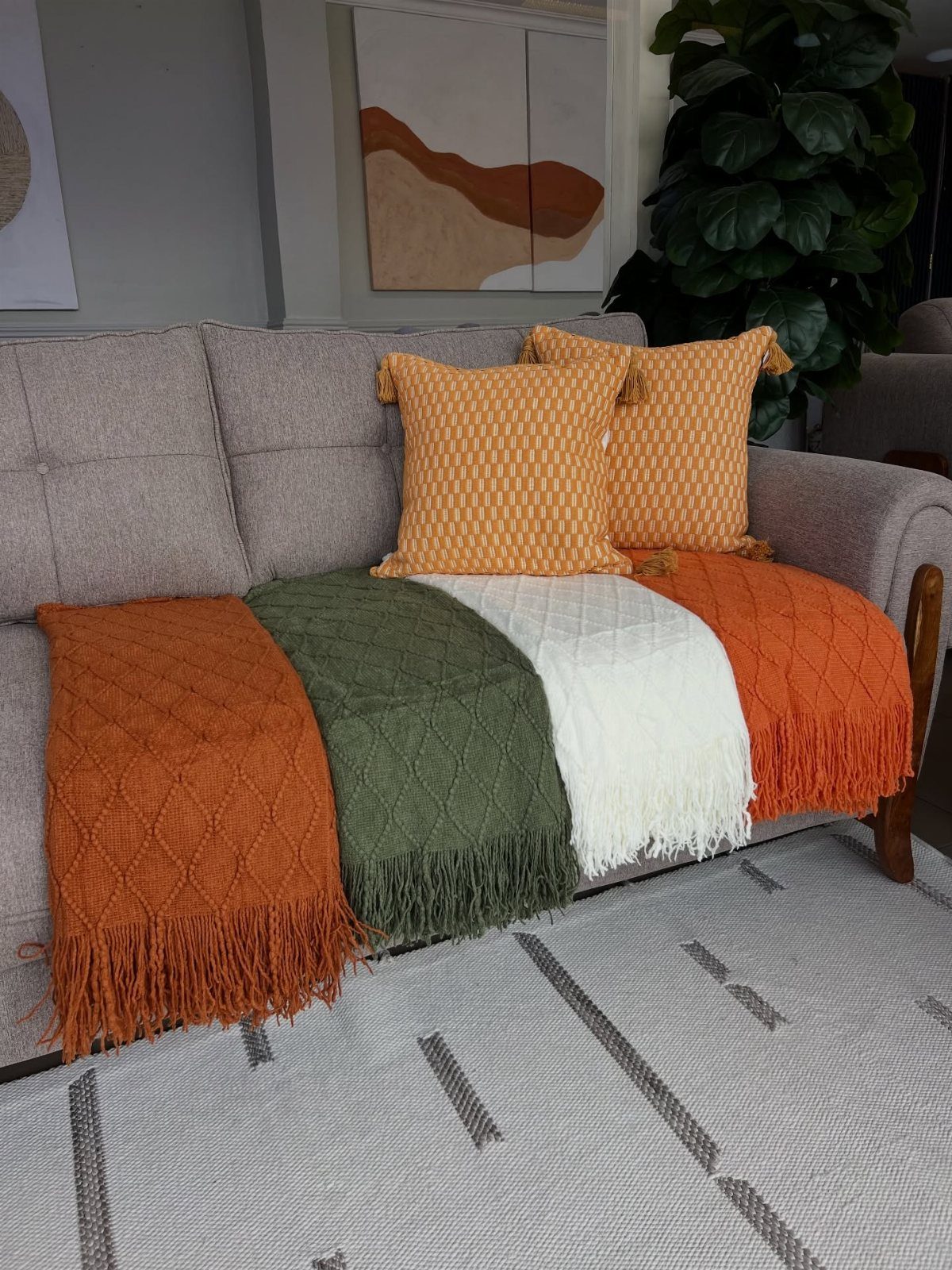 Four colorful textured throw blankets draped over a grey sofa with yellow cushions.