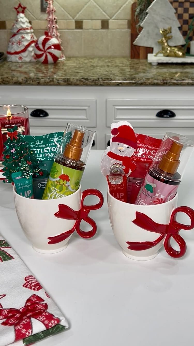 Two white mugs with red bow handles filled with beauty gift products.