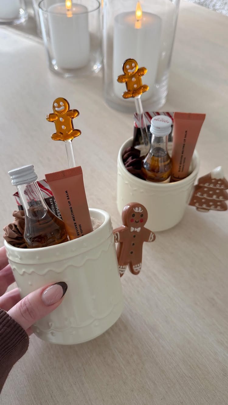 White ceramic mugs filled with syrup bottles and gingerbread stirrers as Christmas gifts.