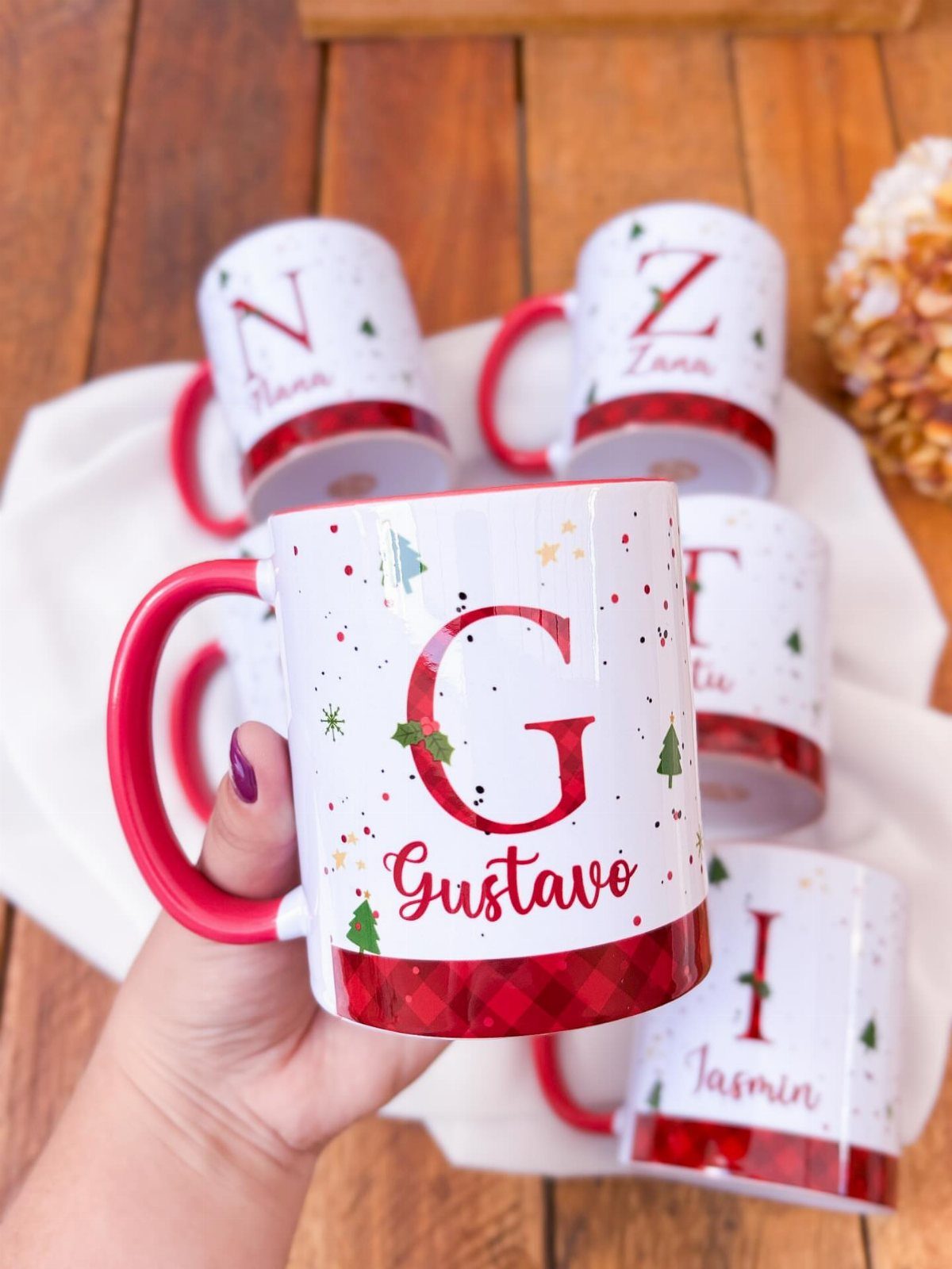 Personalized white Christmas mugs with red accents and names on a wooden table