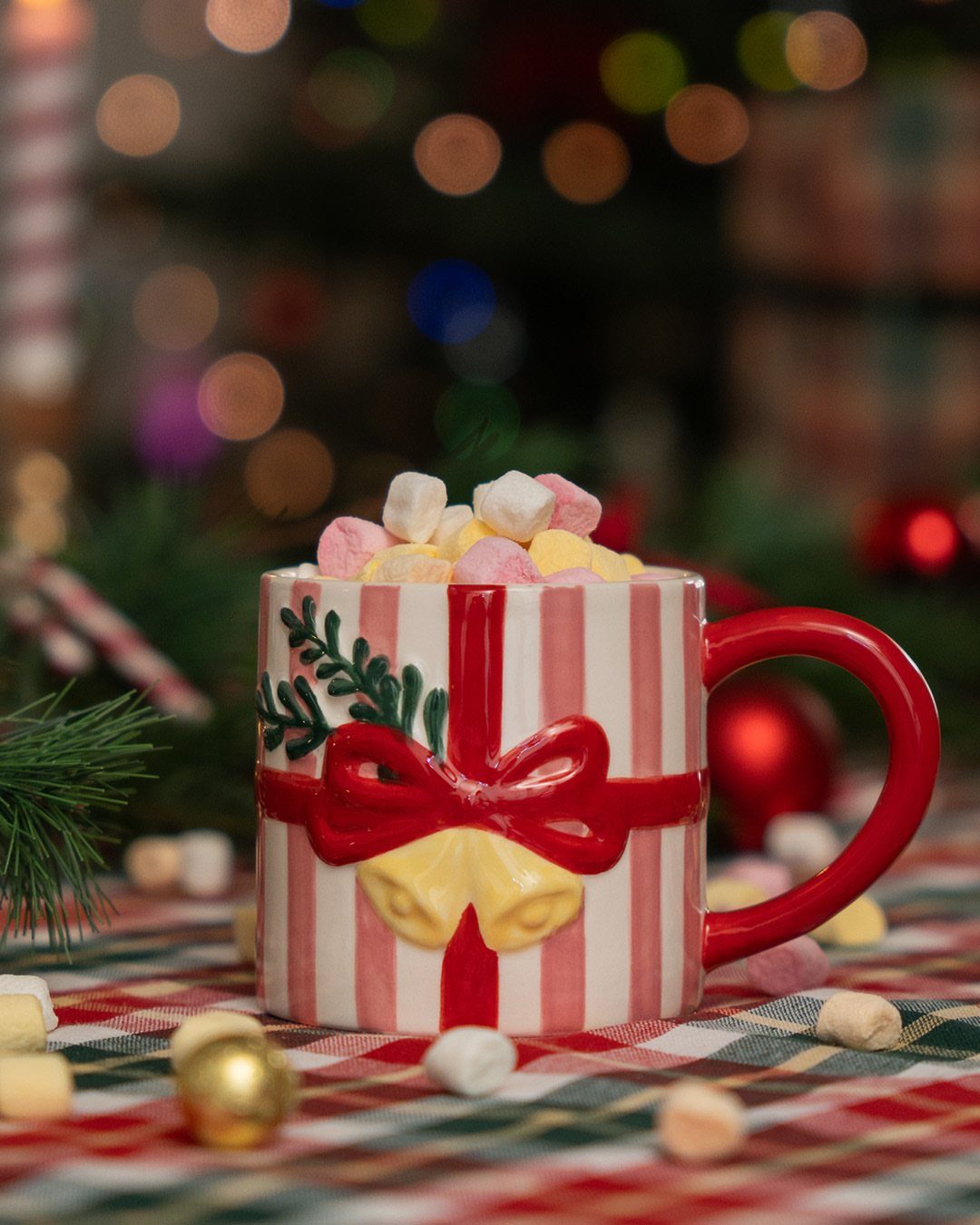 Red and white striped gift-shaped mug filled with marshmallows on plaid fabric.