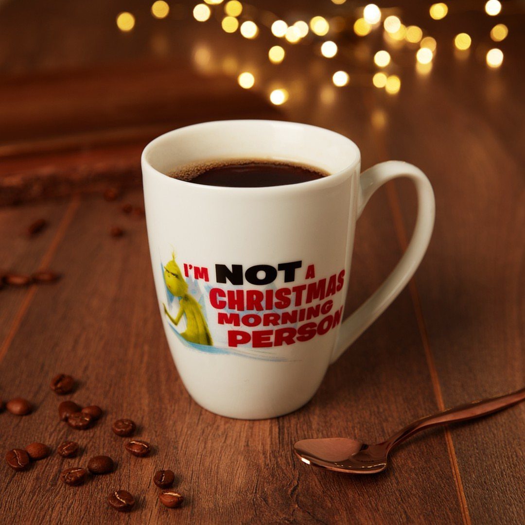 White coffee mug with Grinch illustration and text on a wooden table