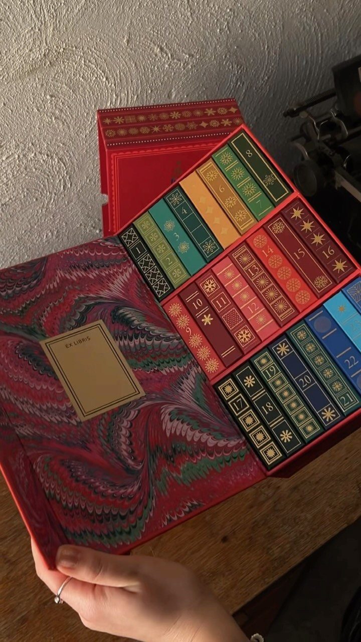 Red book-themed advent calendar with colorful numbered doors held by a hand.