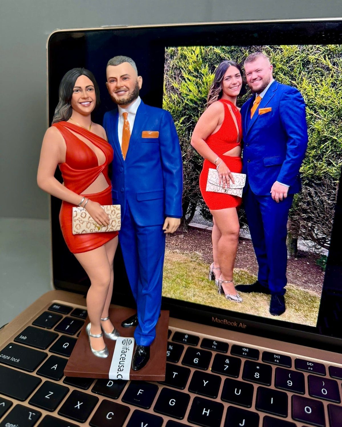 Custom 3D couple figurines standing on a laptop keyboard in front of their photo.