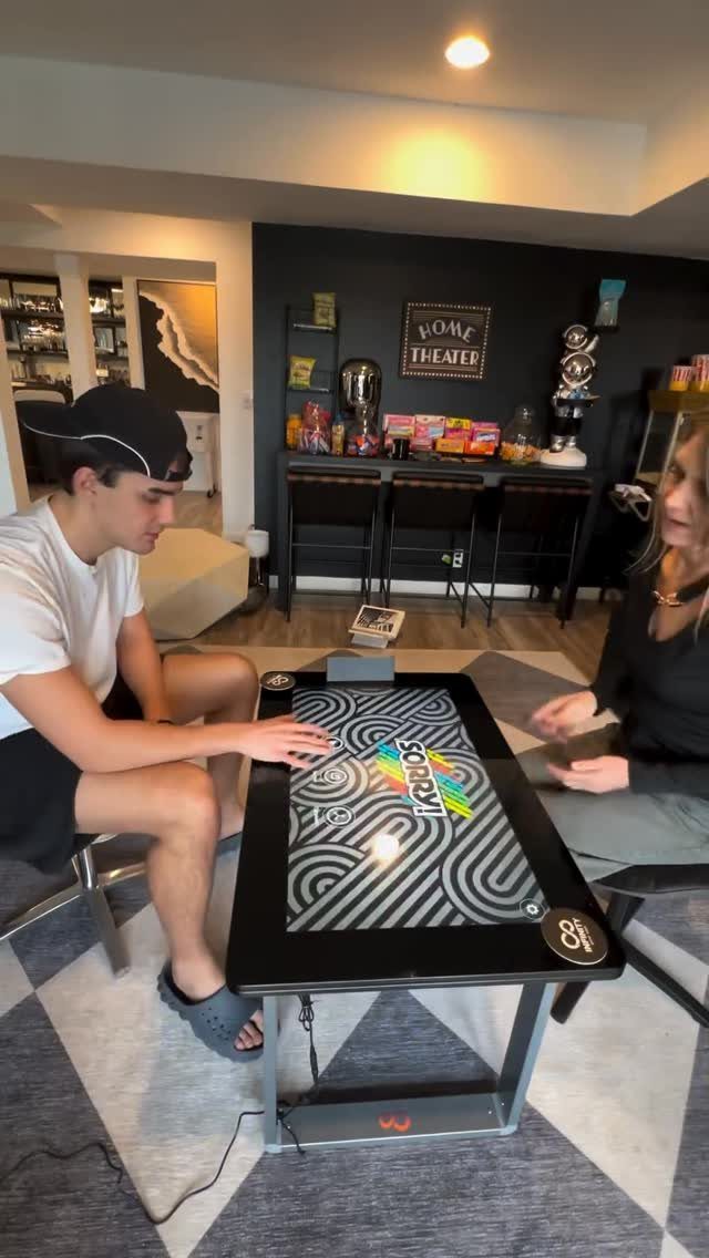 Two people playing a digital game on a sleek black gaming table indoors.