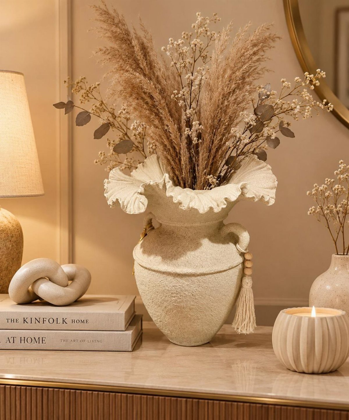 Beige ceramic vase with dried pampas grass, a candle, and books on marble.