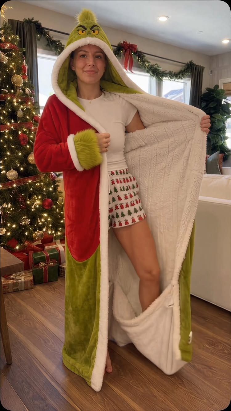 Woman wearing a Grinch wearable blanket standing next to a decorated Christmas tree.
