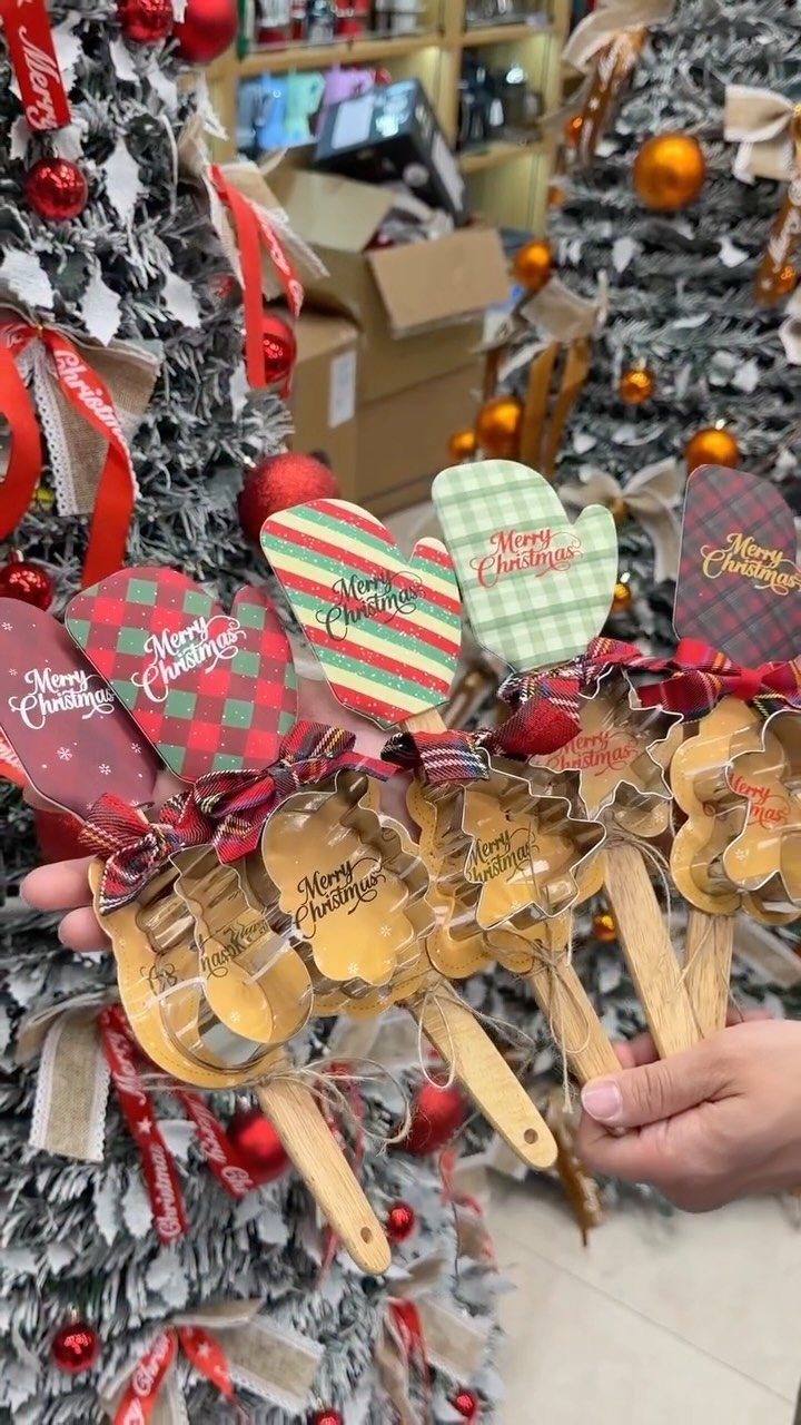 Christmas cookie cutter set with mitten decorations held in front of silver trees