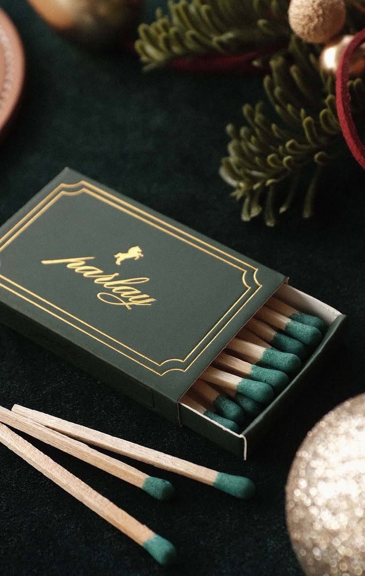 Green matchbox with gold lettering and green-tipped matches among Christmas decorations.