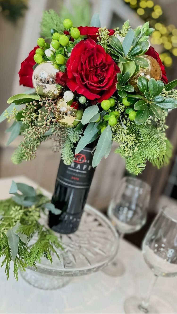 Wine bottle topped with red roses and gold ornaments on a glass pedestal