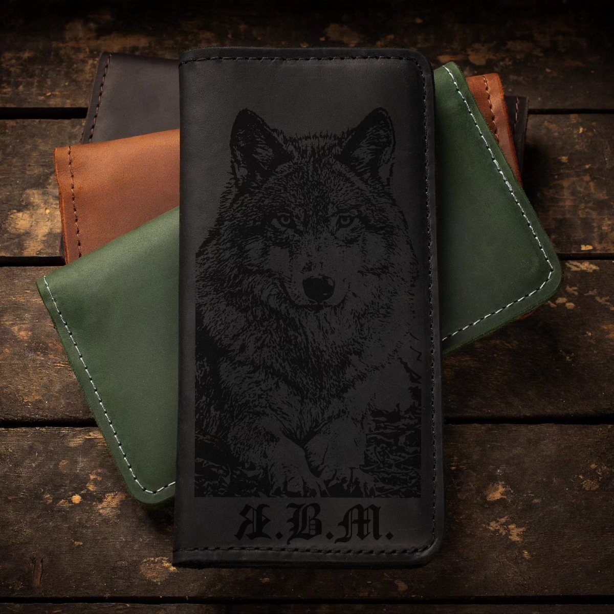 Black leather wallet with engraved wolf and initials on a wooden background