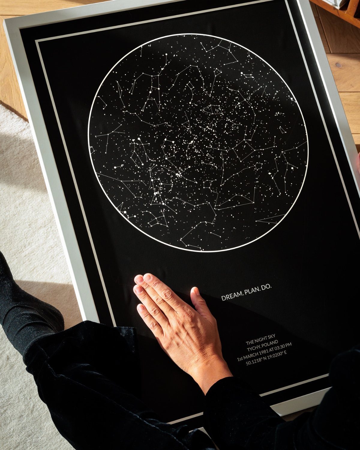 Framed black star map print with white constellations and a person's hand.