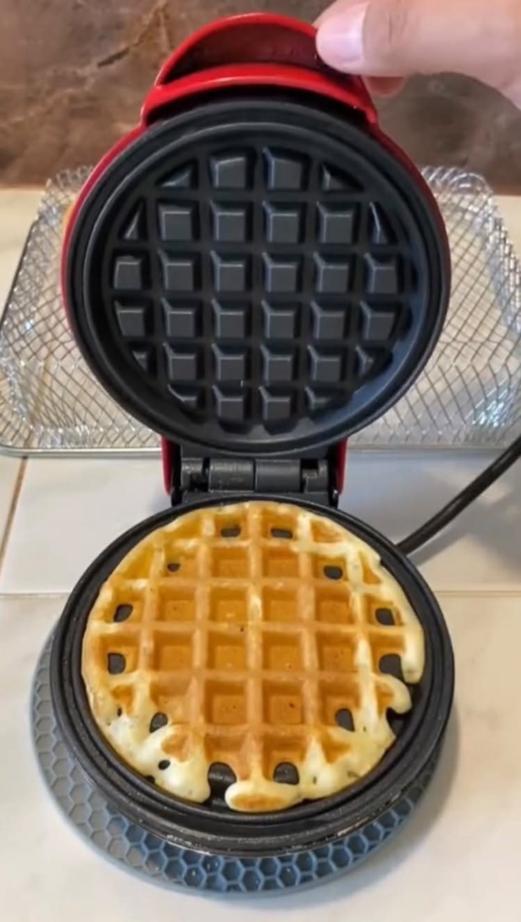 Mini red waffle maker with a freshly cooked golden-brown waffle inside.