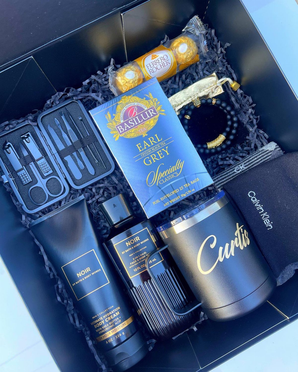 Gift box with grooming products, personalized tumbler, cologne, and chocolates for a man.