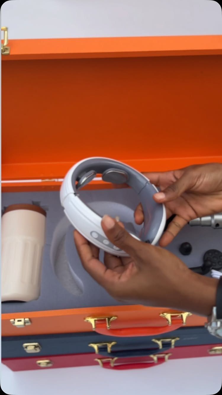 Hands holding a white neck massager inside an orange gift box with a mug.