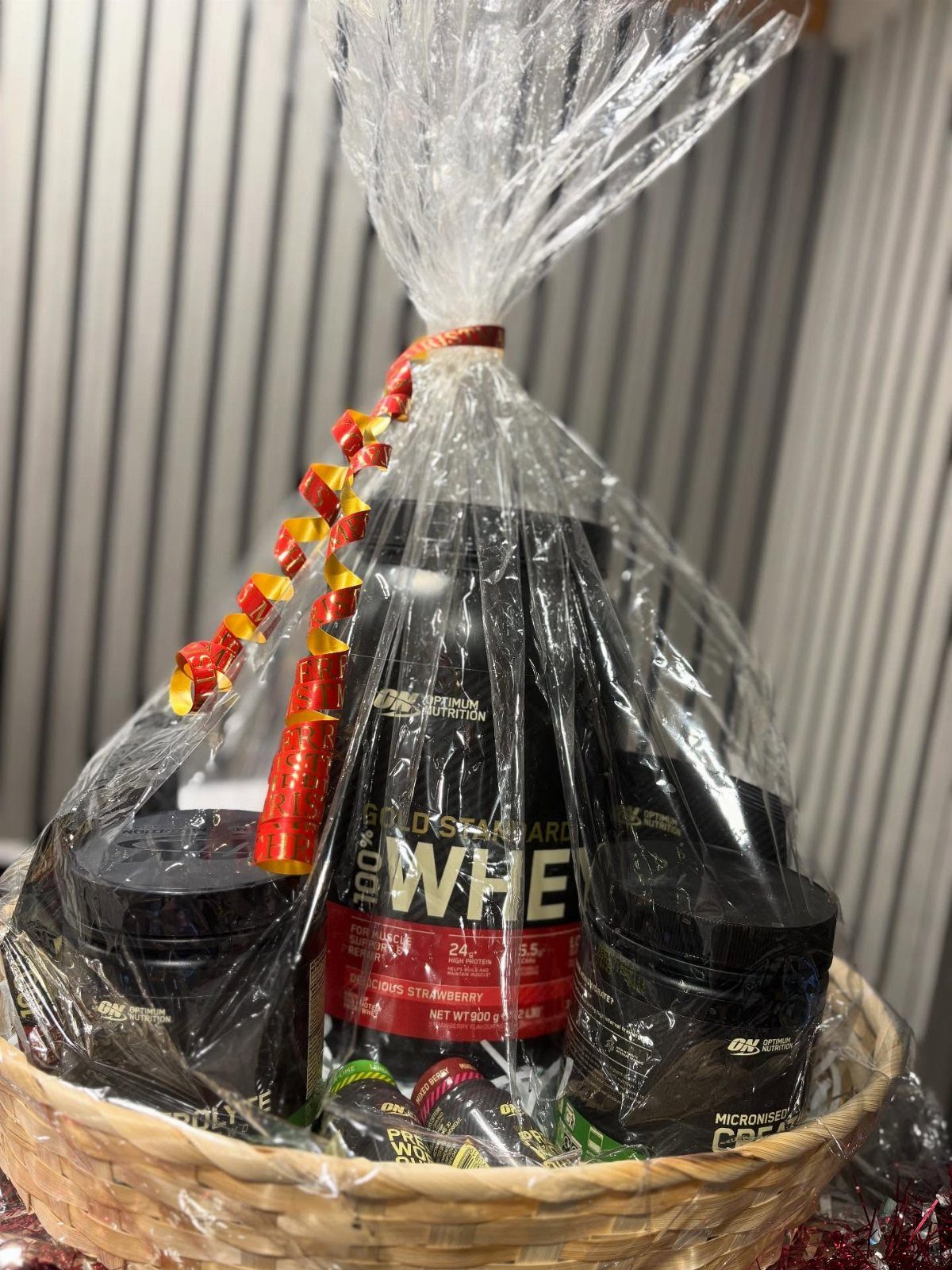Wicker gift basket containing black tubs of whey protein powder wrapped in cellophane