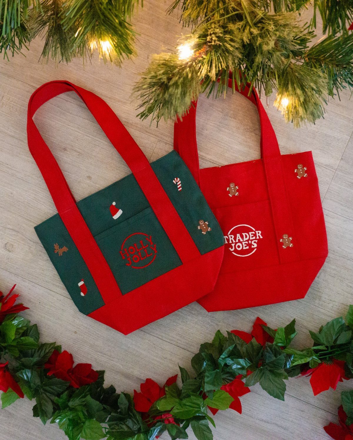 Two red festive Trader Joe's reusable bags surrounded by Christmas greenery and lights.