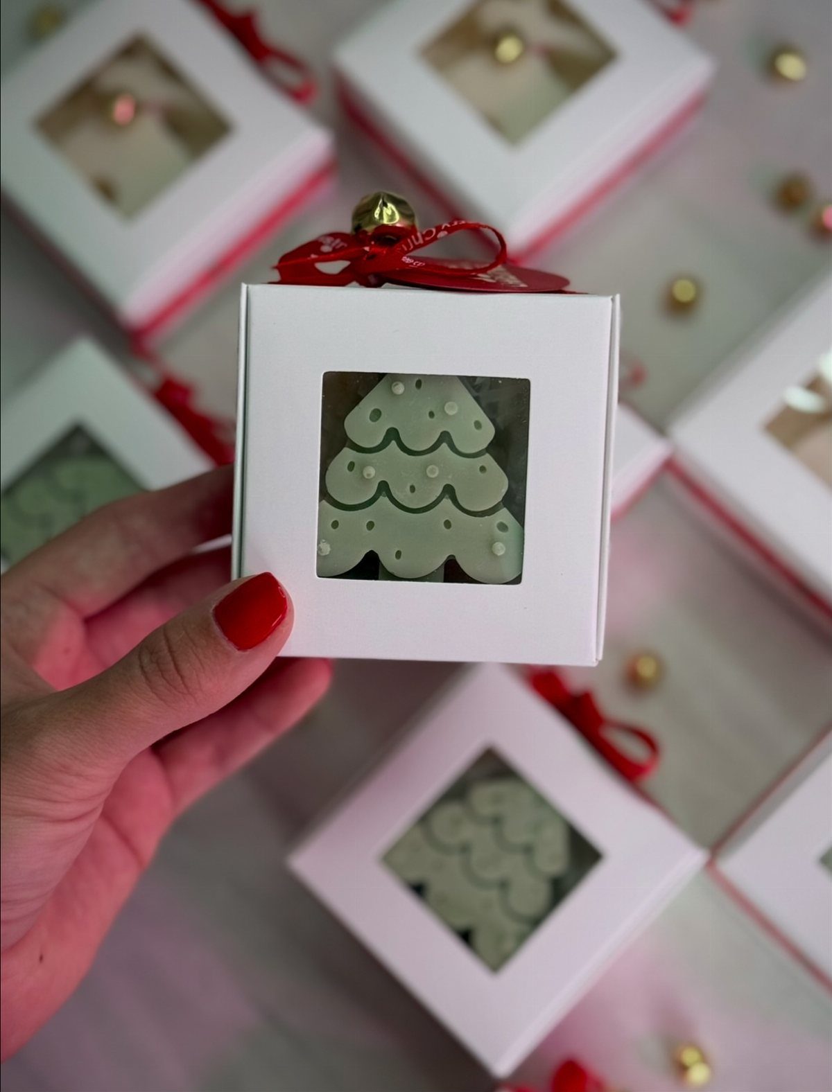 Hand holding a white gift box containing a green Christmas tree shaped cookie