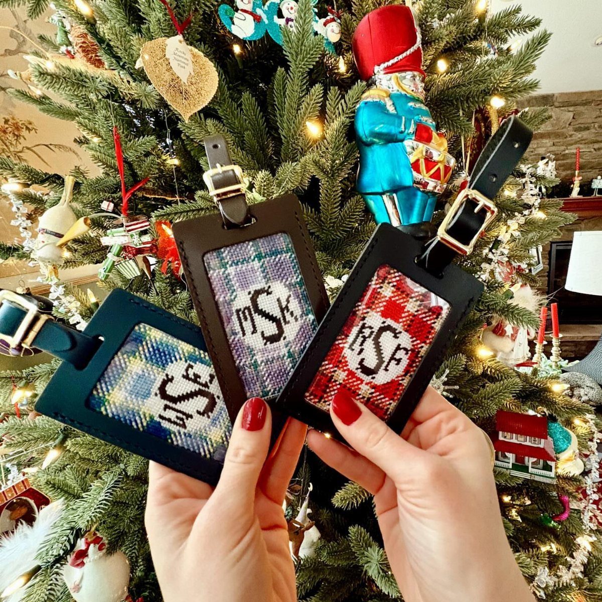 Three monogrammed leather luggage tags held in front of a lit Christmas tree.