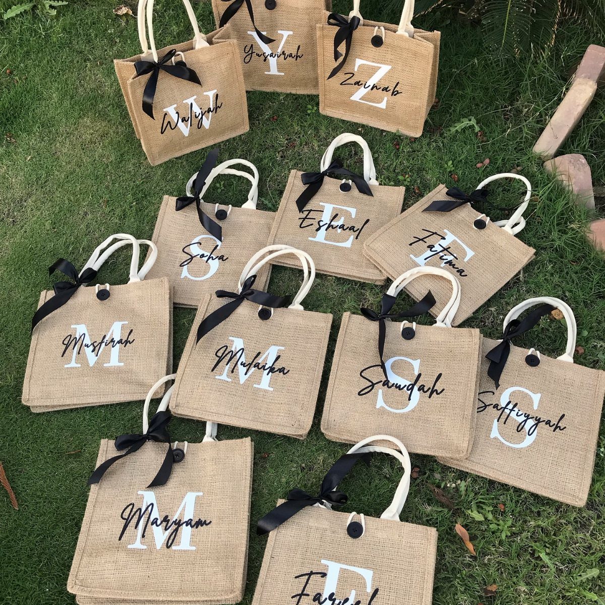 Burlap gift bags with personalized names and initials arranged on green grass.