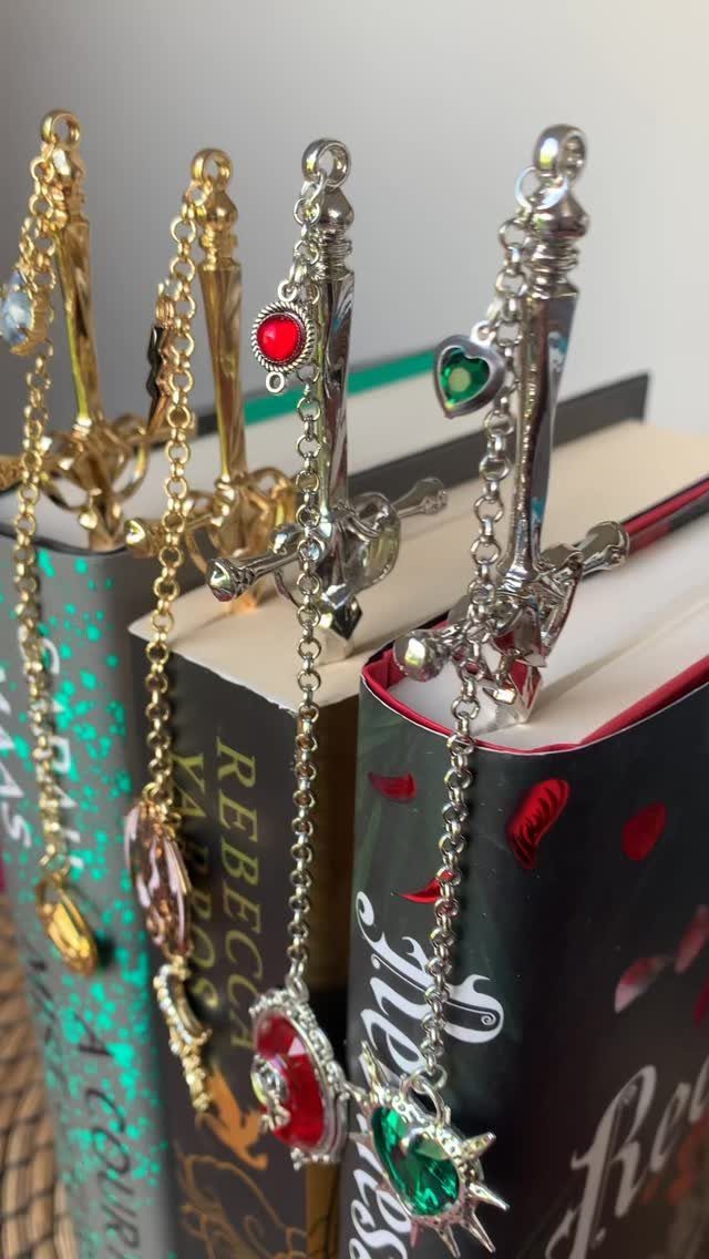 Sword-shaped metal bookmarks with colorful gems placed inside hardcover books.