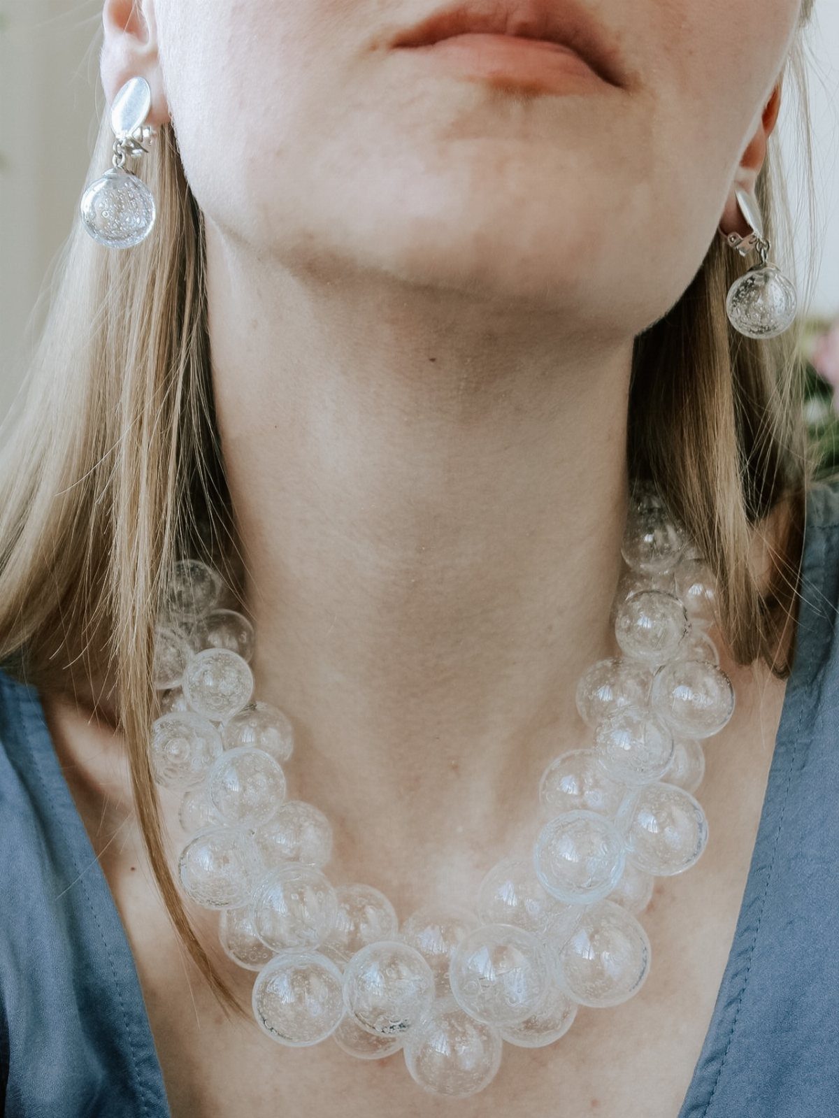 Woman wearing a chunky clear bubble necklace and matching circular drop earrings.