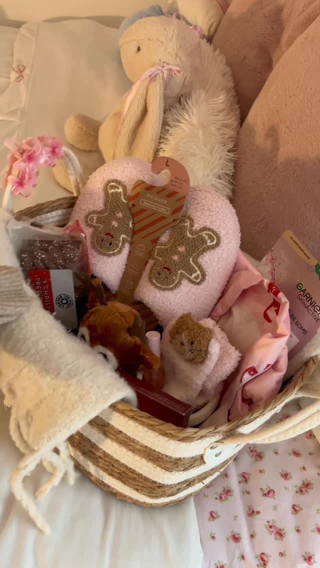 Gift basket with pink gingerbread slippers, plush bunny, and skincare on floral fabric.