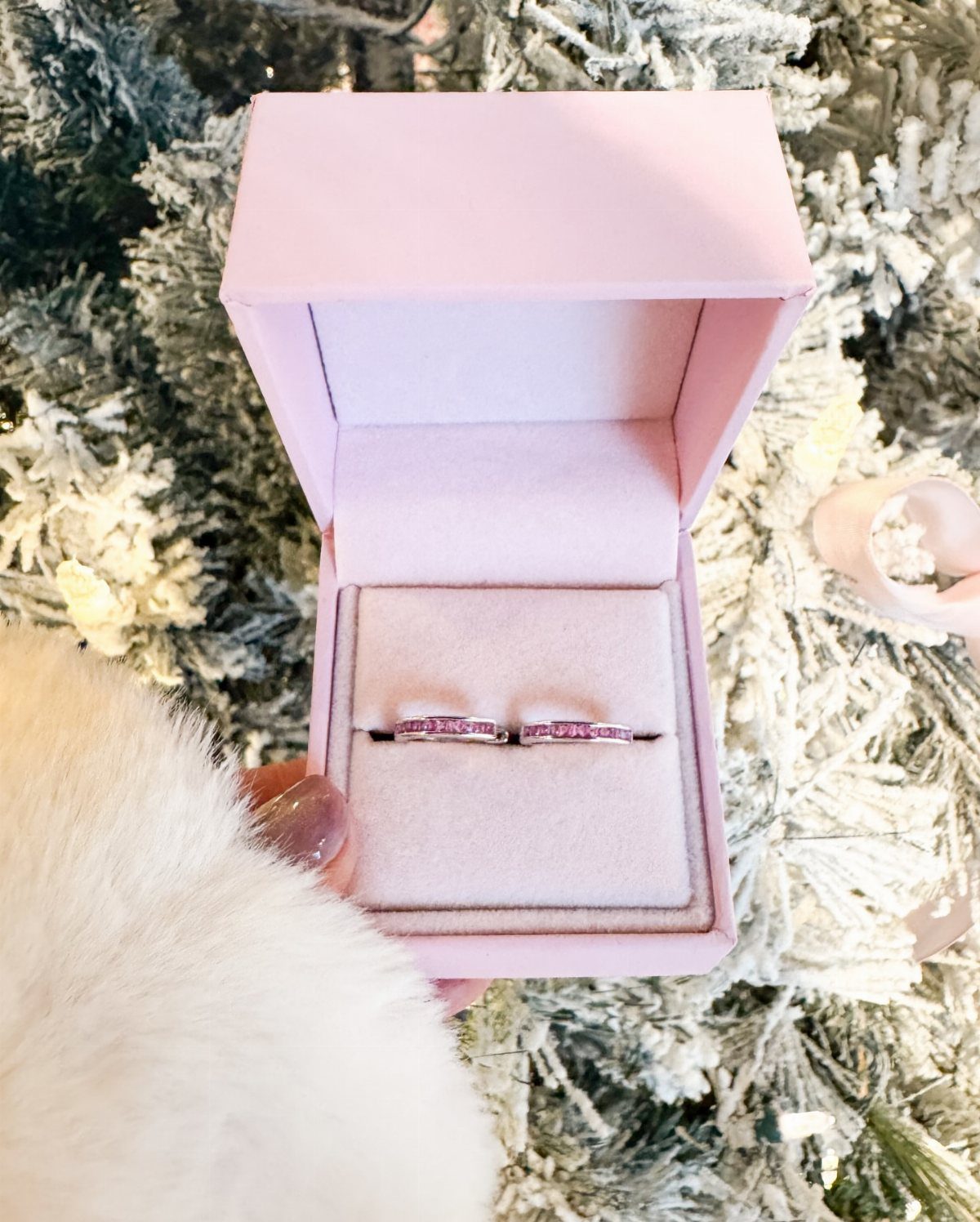 Two silver rings with pink stones in a pink box against snowy branches.