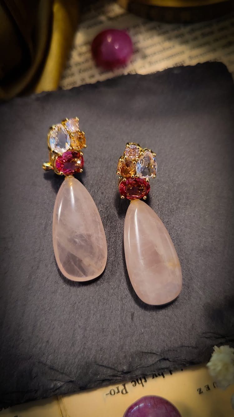 Gold earrings with pale pink teardrop stones and red gemstones on dark fabric