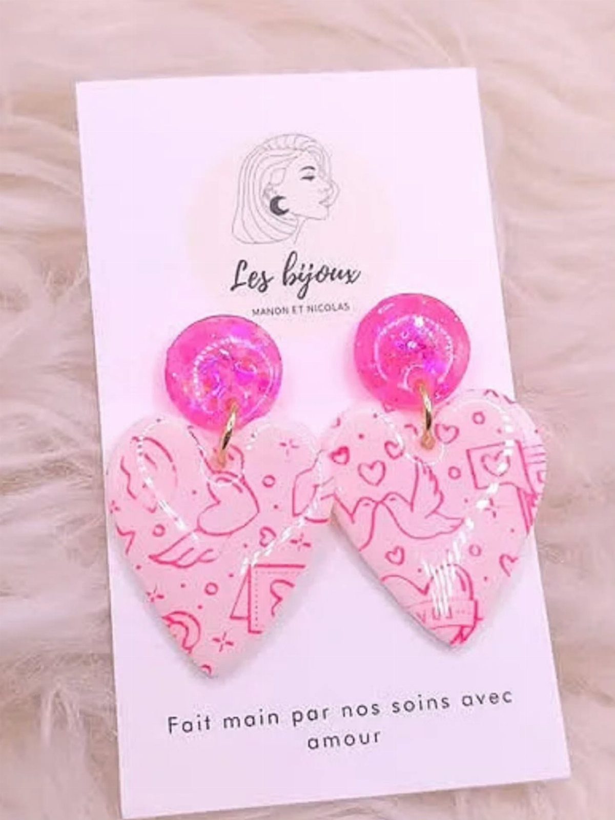 Pink heart-shaped earrings with illustrations on a white display card and faux fur.